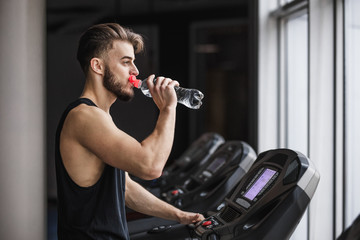 Portrait of handsome sportsman making cardio workout and drinking water in the gym