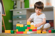 © Serhii - Adorable little boy playing with building cubes at home, laying on floor.