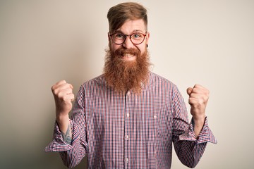 Sticker - Handsome Irish redhead business man with beard wearing glasses over isolated background celebrating surprised and amazed for success with arms raised and open eyes. Winner concept.