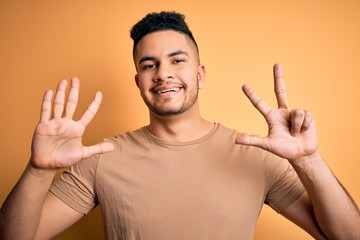 Young handsome man wearing casual t-shirt standing over isolated yellow background showing and pointing up with fingers number eight while smiling confident and happy.