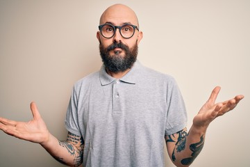 Wall Mural - Handsome bald man with beard and tattoo wearing casual polo and glasses clueless and confused expression with arms and hands raised. Doubt concept.