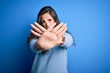 © Krakenimages.com - Young beautiful woman with curly hair wearing blue casual sweater over isolated background Rejection expression crossing arms and palms doing negative sign, angry face