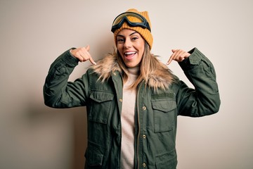 Sticker - Young brunette skier woman wearing snow clothes and ski goggles over white background looking confident with smile on face, pointing oneself with fingers proud and happy.