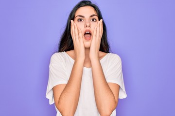 Poster - Young beautiful brunette woman wearing casual white t-shirt over purple background afraid and shocked, surprise and amazed expression with hands on face