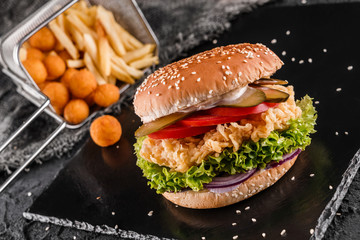 Wall Mural - Chicken burger with tomatoes, lettuce, sauce and fried stick balls, french fries on slate black background, close up