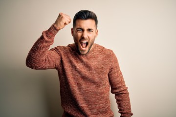 Sticker - Young handsome man wearing casual sweater standing over isolated white background angry and mad raising fist frustrated and furious while shouting with anger. Rage and aggressive concept.