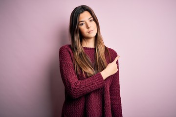 Sticker - Young beautiful girl wearing casual sweater over isolated pink background Pointing with hand finger to the side showing advertisement, serious and calm face