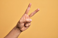 Hand Of Caucasian Young Man Showing Fingers Over Isolated Yellow Background Counting Number 2 Showing Two Fingers, Gesturing Victory And Winner Symbol