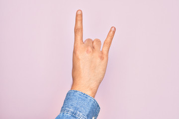 Hand of caucasian young man showing fingers over isolated pink background gesturing rock and roll symbol, showing obscene horns gesture