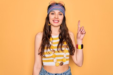 Wall Mural - Young beautiful hippie woman with blue eyes wearing accesories and sunnglasses showing and pointing up with finger number one while smiling confident and happy.