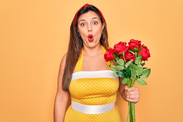 Young hispanic pin up woman wearing fashion sexy 50s style holding bouquet of red roses scared in shock with a surprise face, afraid and excited with fear expression