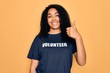 Young african american curly woman doing volunteering wearing volunteer t-shirt happy with big smile doing ok sign, thumb up with fingers, excellent sign