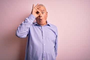 Middle age handsome hoary man wearing casual shirt standing over pink background doing ok gesture shocked with surprised face, eye looking through fingers. Unbelieving expression.