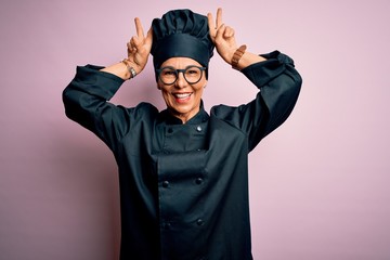 Middle age brunette chef woman wearing cooker uniform and hat over isolated pink background Posing funny and crazy with fingers on head as bunny ears, smiling cheerful