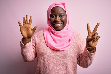 Canvas Print - Young african american plus size woman wearing muslim hijab over isolated pink background showing and pointing up with fingers number seven while smiling confident and happy.