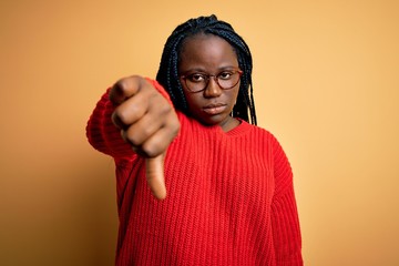 Poster - African american plus size woman with braids wearing casual sweater over yellow background looking unhappy and angry showing rejection and negative with thumbs down gesture. Bad expression.