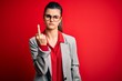 Young beautiful brunette businesswoman wearing jacket and glasses over red background Showing middle finger, impolite and rude fuck off expression
