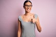 © Krakenimages.com - Young beautiful woman wearing casual striped dress and glasses over pink background doing happy thumbs up gesture with hand. Approving expression looking at the camera showing success.