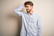 © Krakenimages.com - Young handsome man with beard wearing striped shirt standing over white background smiling confident touching hair with hand up gesture, posing attractive and fashionable