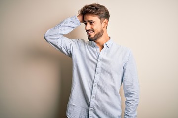 Young handsome man with beard wearing striped shirt standing over white background smiling confident touching hair with hand up gesture, posing attractive and fashionable