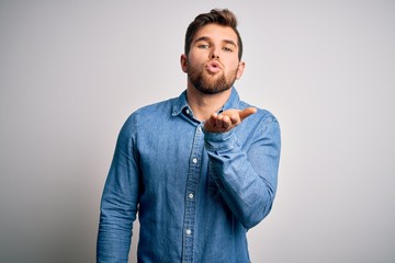 Wall Mural - Young handsome blond man with beard and blue eyes wearing casual denim shirt looking at the camera blowing a kiss with hand on air being lovely and sexy. Love expression.