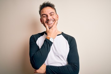 Young handsome man wearing casual t-shirt standing over isolated white background looking confident at the camera smiling with crossed arms and hand raised on chin. Thinking positive.