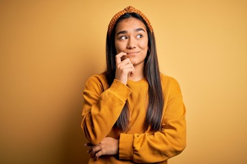 Canvas Print - Young beautiful asian woman wearing casual sweater and diadem over yellow background with hand on chin thinking about question, pensive expression. Smiling with thoughtful face. Doubt concept.