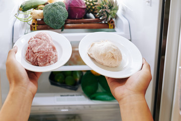 Woman putting plates with ground pork and chicken in refrigerator