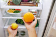 © DragonImages - Woman taking citrus fruits: orange and lemon out of refrigerator when searching for snacks at home