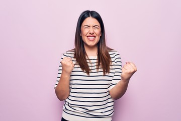 Poster - Young beautiful brunette woman wearing casual striped t-shirt over isolated pink background celebrating surprised and amazed for success with arms raised and eyes closed