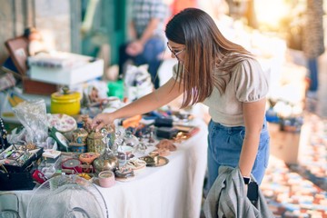 Young beautiful woman smiling happy and confident. Standing with smile on face looking a jumble sale at the town street