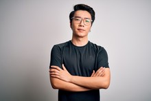 Young Handsome Chinese Man Wearing Black T-shirt And Glasses Over White Background Skeptic And Nervous, Disapproving Expression On Face With Crossed Arms. Negative Person.