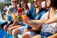 Close View. Friends Clinking Glasses With Fresh Colorful Cocktails Sitting By Swimming Pool On Sunny Summer Day. People Toast Drinking Beverages At Luxury Villa Poolside Party On Tropical Vacation.
