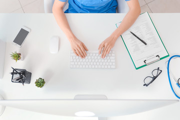 Female doctor working on computer in clinic, top view