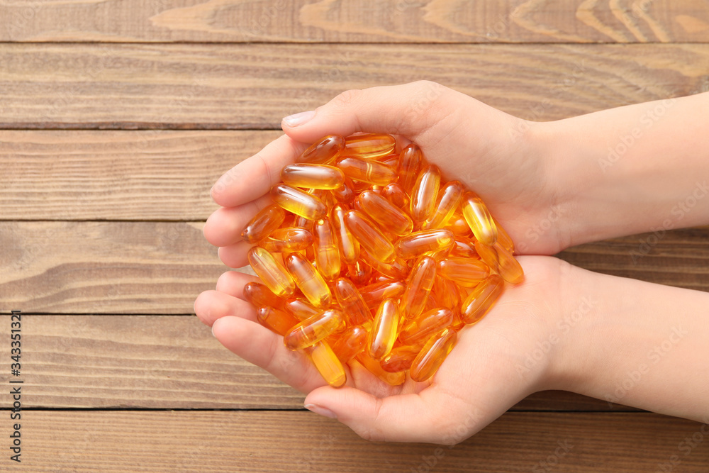 Female hands with fish oil capsules on wooden background