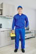 © DragonImages - Smiling Asian handyman in blue uniform holding toolbox and smiling at camera