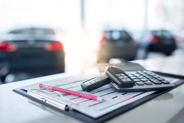 New key - images of car showrooms with calculators and two new remote keys placed on the work table in the new car showroom. The background is a car showroom.