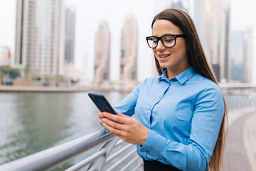 Young pretty business woman texting on a mobile phone outdoors on skyscrapers background