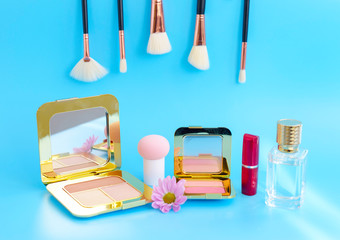 premium makeup brushes, red lipstick, bottle of perfume and blush pads on a bright blue background, creative cosmetics flat lay