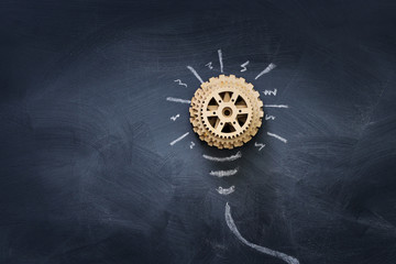 Wall Mural - Education concept image. Creative idea and innovation. Wooden gears light bulb metaphor over blackboard