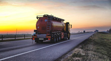 A Truck Carries A Tank Of Combustible Fuel On A Highway Against A Forest And Blue Sky. The Concept Of Transportation Of Dangerous Goods On The Road, License, Sunset
