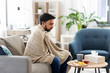 © Syda Productions - health, cold and people concept - sick young indian man in blanket with hot tea with lemon, honey and ginger at home