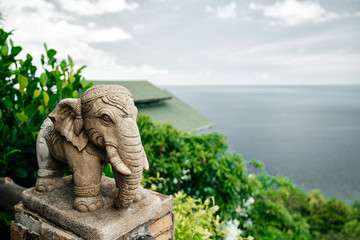 Stone statue of an elephant in tropical greenery and sea view.