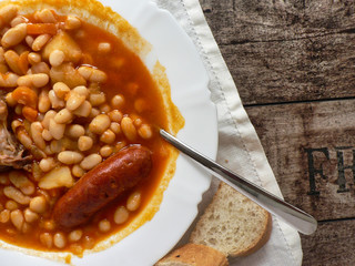 Canvas Print - Spanish Asturian fabada in a white plate, spoon on wooden table