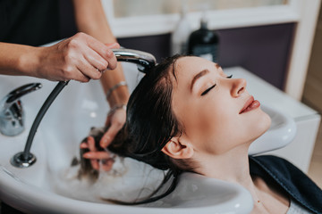 Wall Mural - Professional hairdresser washing hair of a beautiful young  woman in hair salon. .