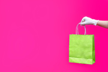 Woman hand in glove with paper bag on pink background. Delivery of food, groceries, home shopping. Protection for COVID-19 Coronavirus precautions.