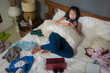 slackness and disorganized during covid-19 home lockdown - young disorderly and chaotic Asian Chinese woman on bed using internet mobile phone on grimy messy bedroom