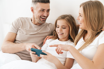 Wall Mural - Photo of girl playing video game on cellphone with parents in bad