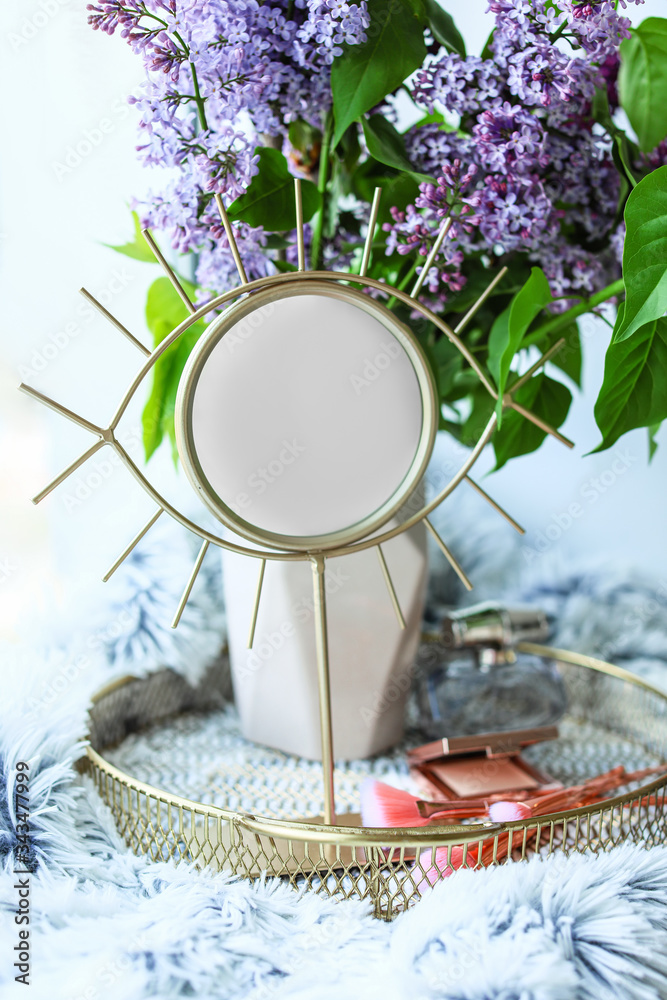 Vase with beautiful lilac flowers, makeup cosmetics and mirror on window sill