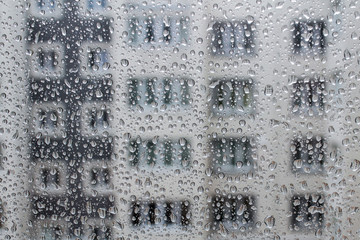 Rain drops on the glass as background, silhouette of modern condominium facade behind the window on rainy days